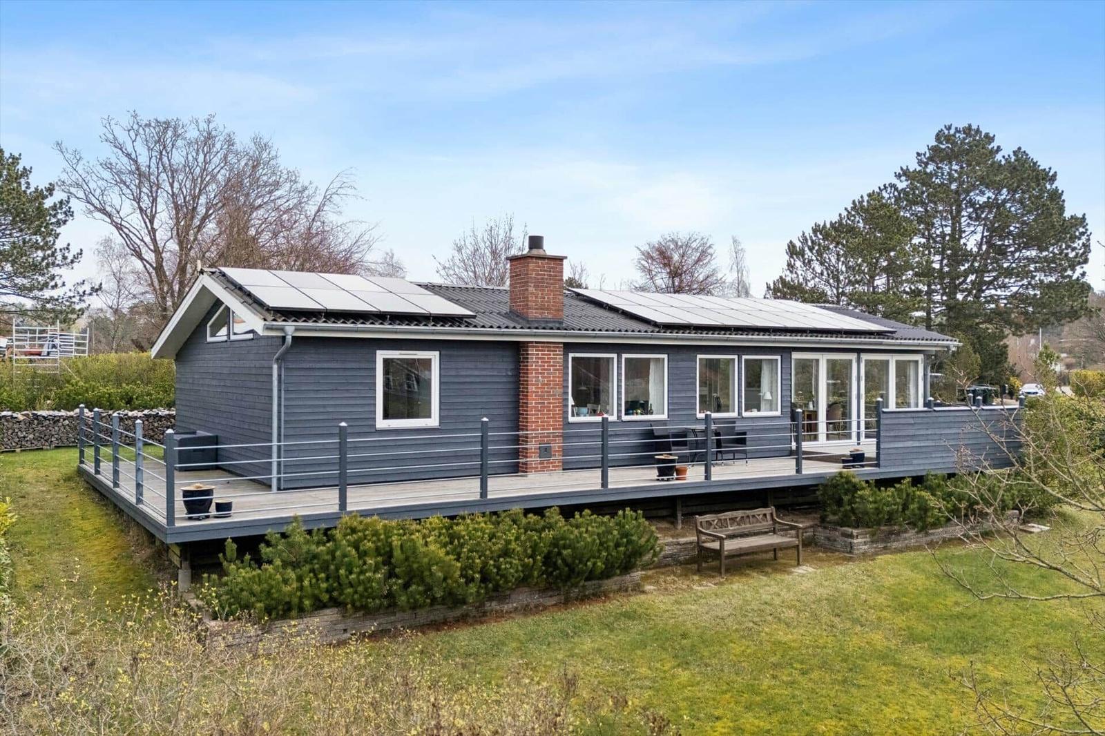 Ein modernes Haus mit Terrasse und Solarpanelen. Umgeben von Grün und Bäumen.