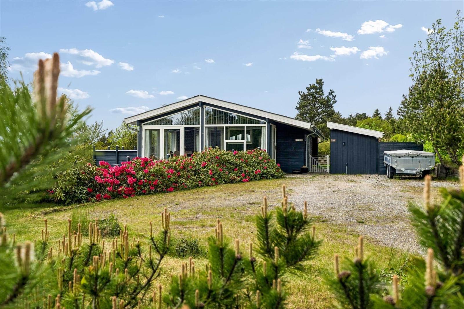 Moderne Villa mit großem Garten und blühenden Sträuchern. Garage und Anhänger sind vorhanden.