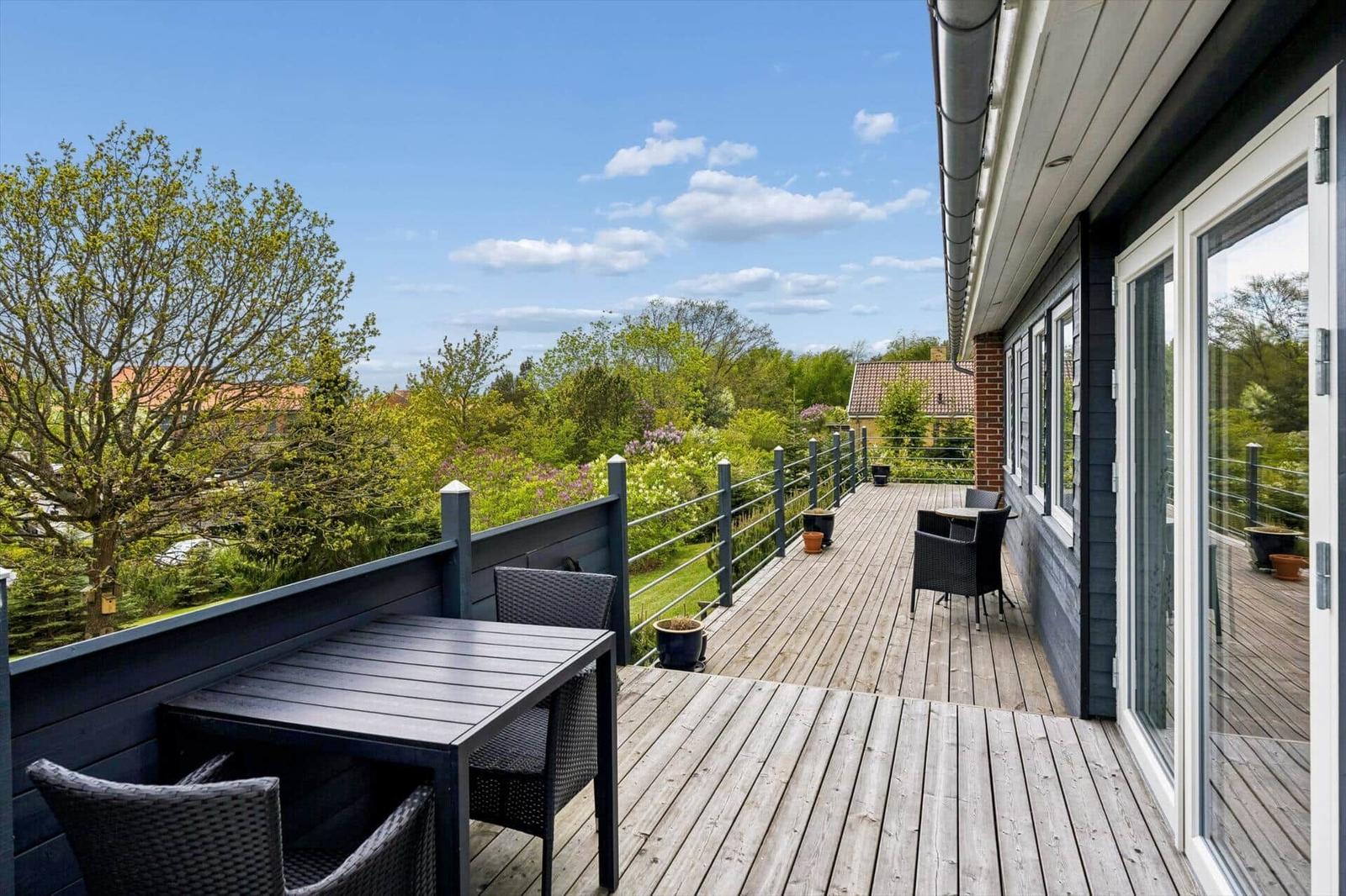 Terrasse mit Tisch und Stühlen, Blick auf grüne Umgebung und Himmel.