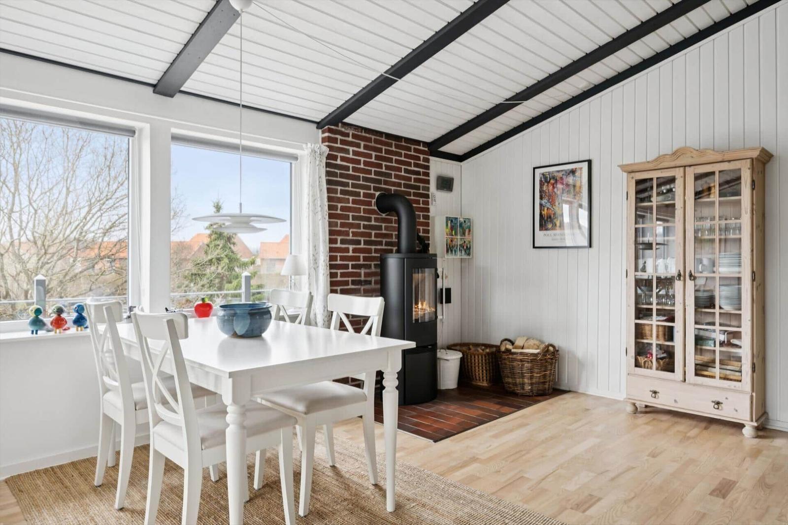 Esszimmer mit weißem Tisch, Stühlen, Kamin und Glasvitrine.