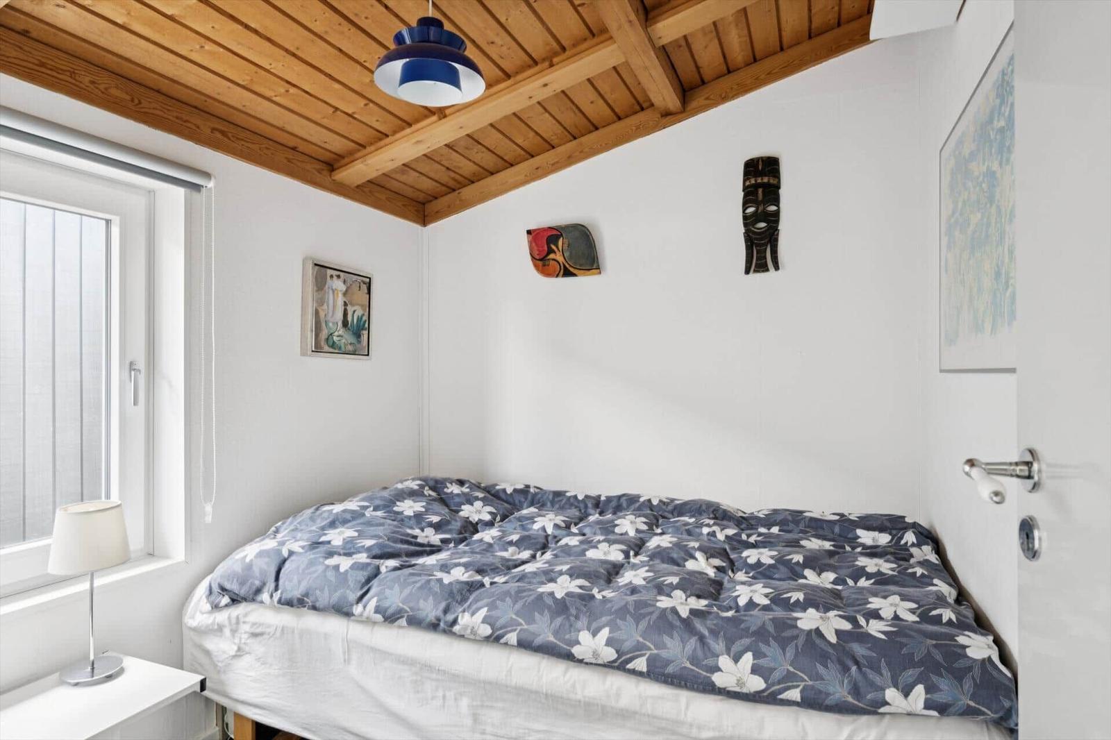 Schlafzimmer mit Bett, Fenster, Lampe und Holzdecke.