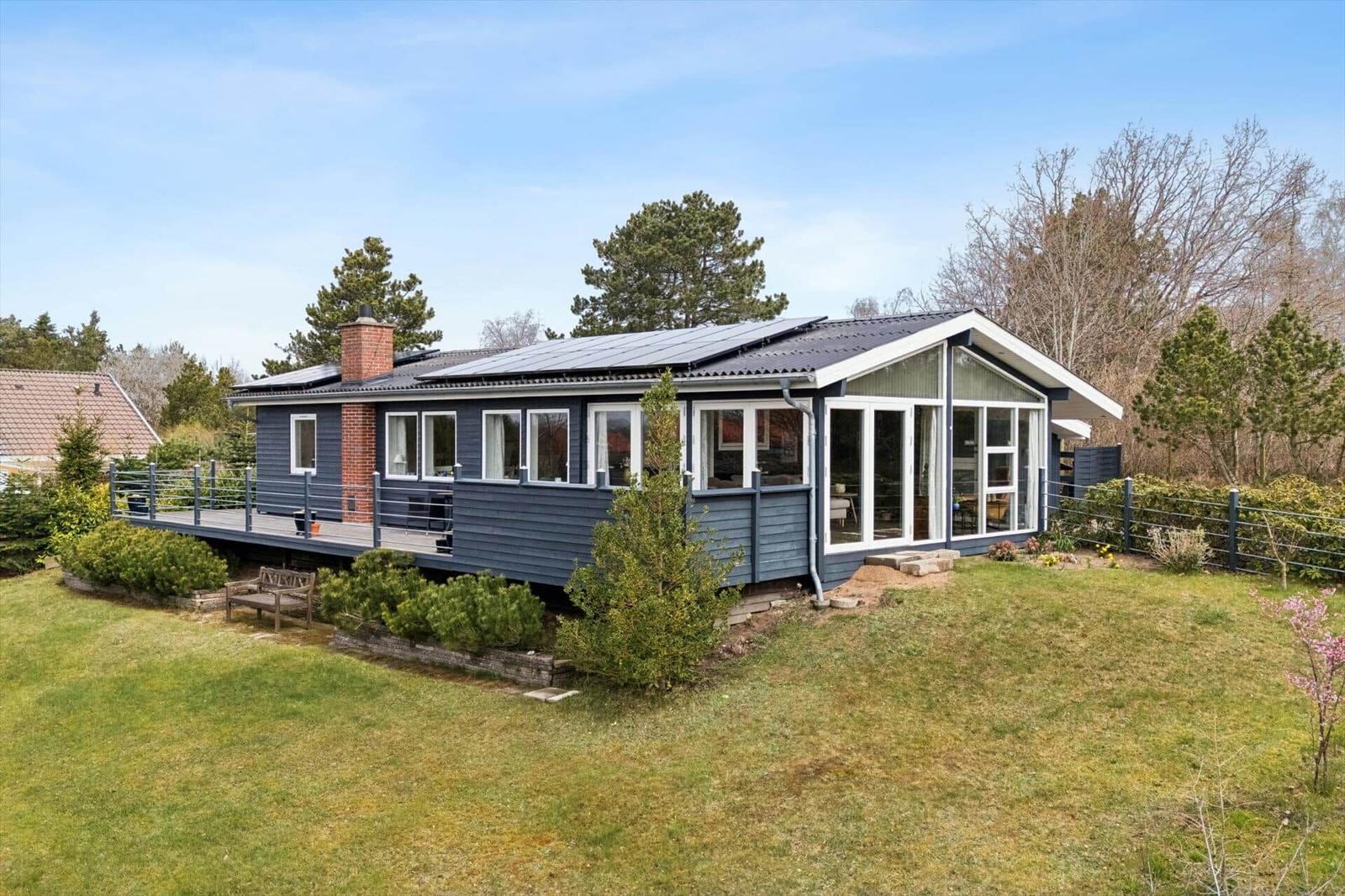 Moderne Ferienhaus mit Terrasse, Solaranlage und Garten. Holzveranda und große Fenster.