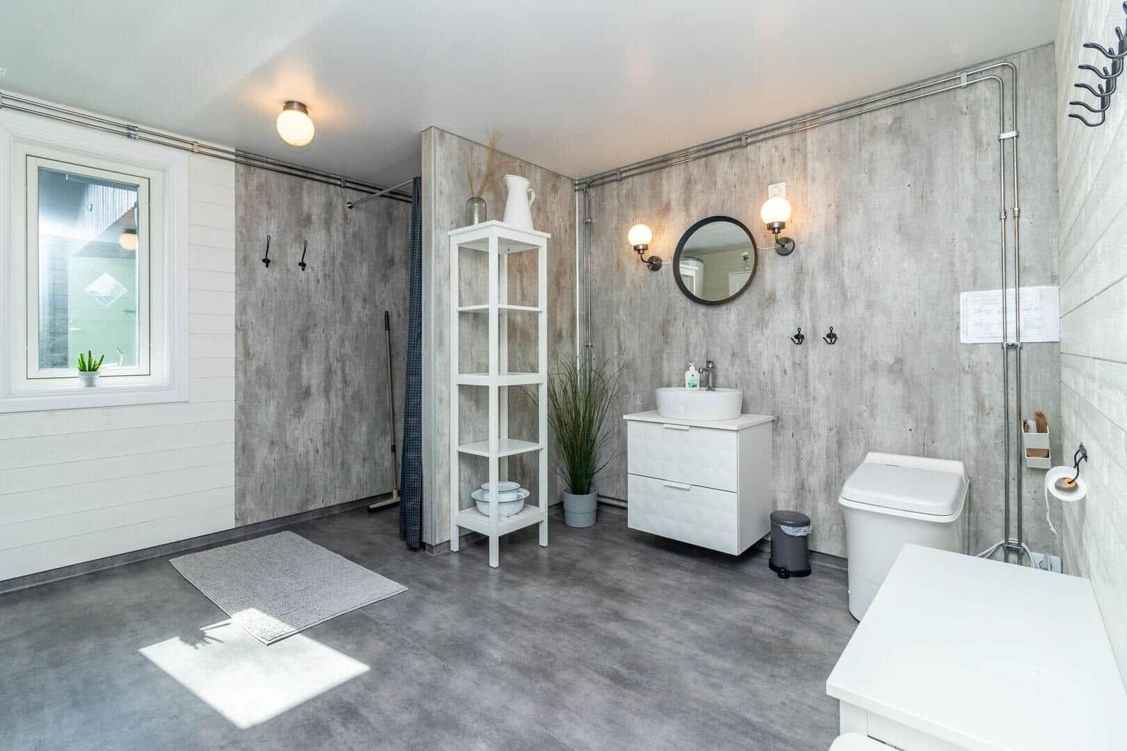 Badezimmer mit Dusche, Waschbecken und Toilette. Holzwand, Fenster und weiße Möbel.