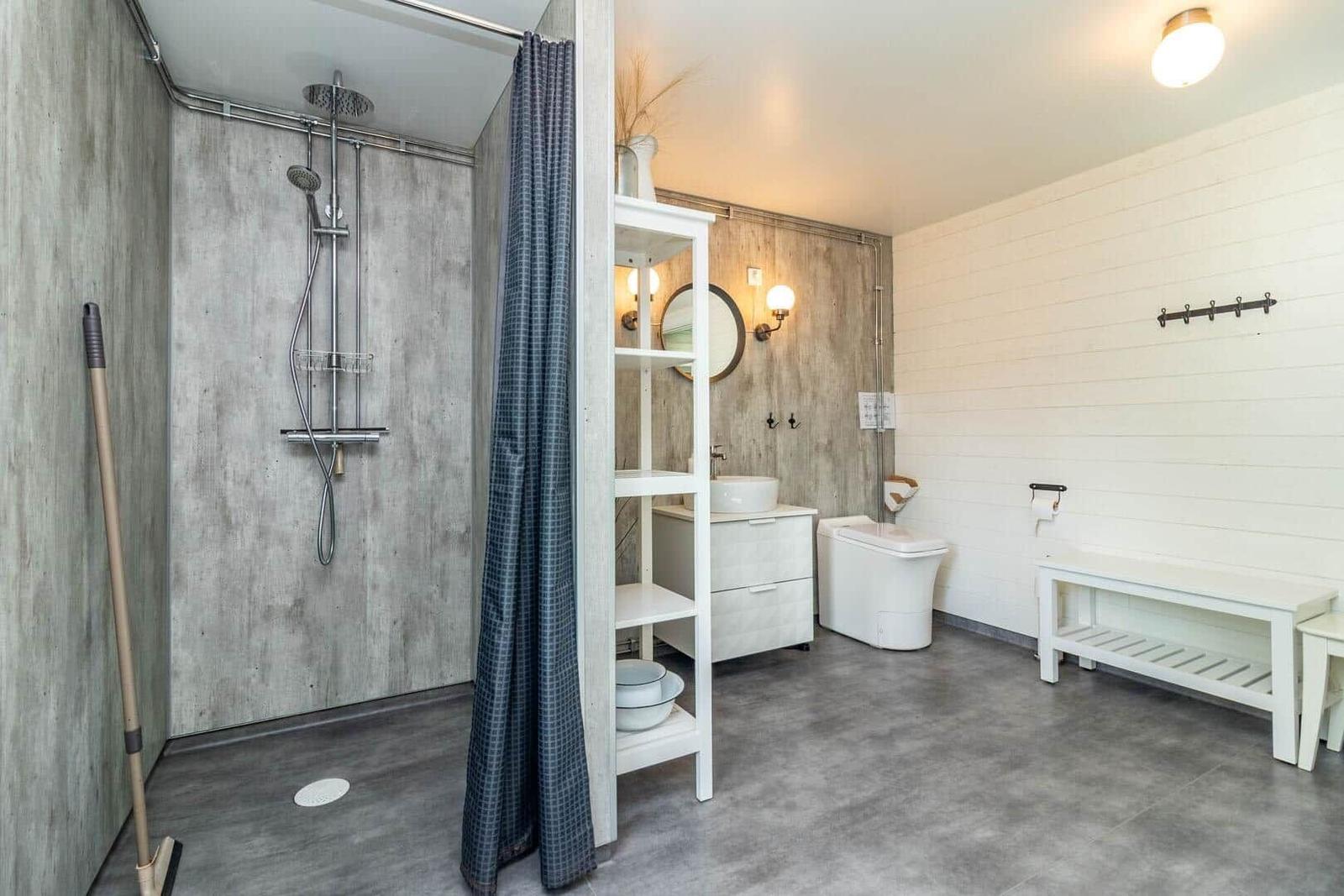 Bad mit Dusche, Waschbecken und Toilette. Weiße Schränke und Holzwände.
