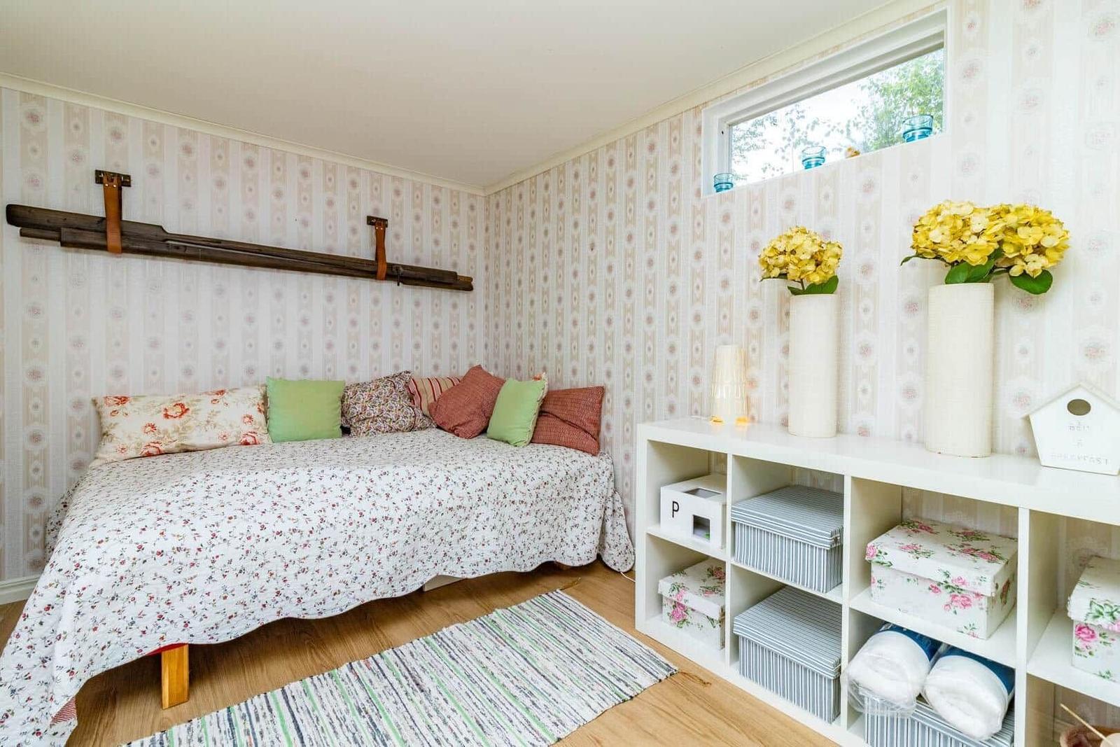 Schlafzimmer mit Bett, Wandpaneelen und Regal mit Blumen.