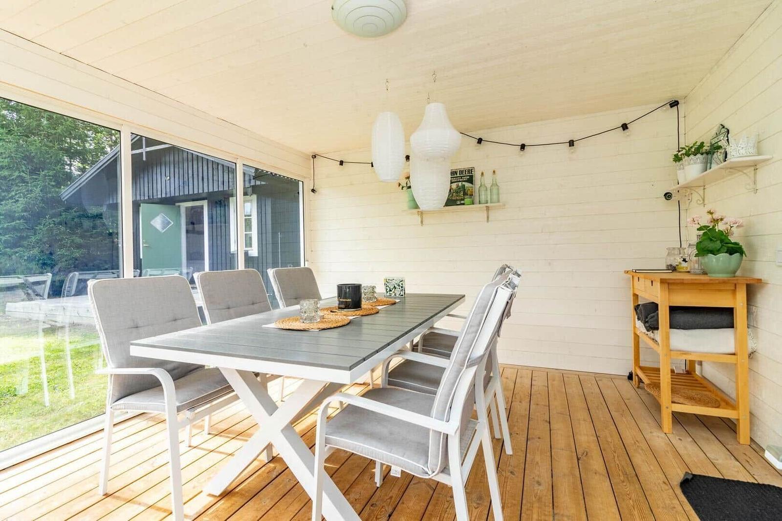 Terrasse mit Esstisch, Stühlen und Lichtern. Holzfußboden und weiße Wände.