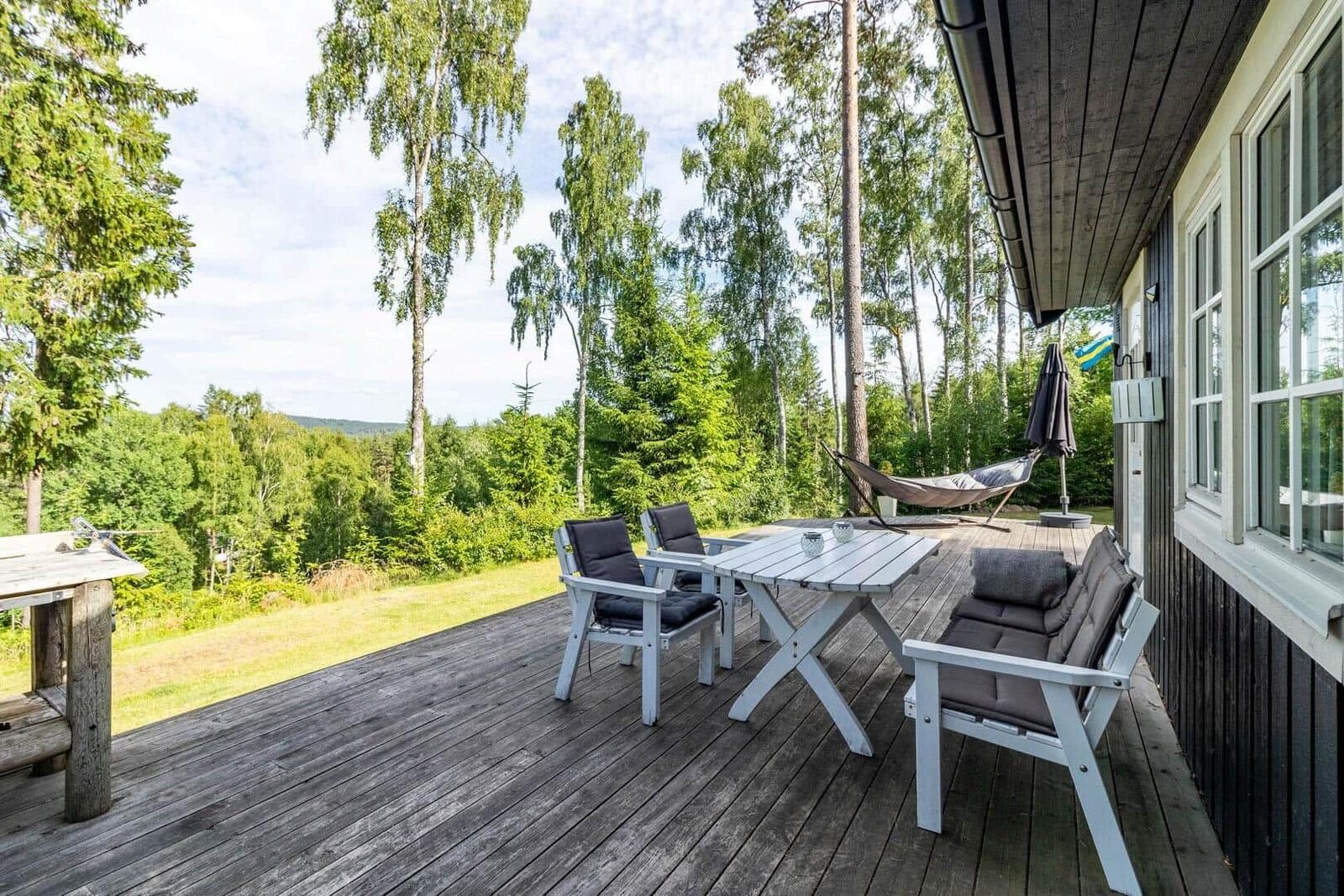 Terrasse mit Tisch, Stühlen und Hängematte. Blick auf Wald und Grasfläche.