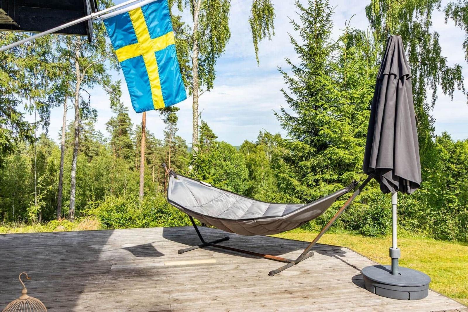 Hammock auf Holzterrasse mit schwedischer Flagge und geschlossenem Sonnenschirm.