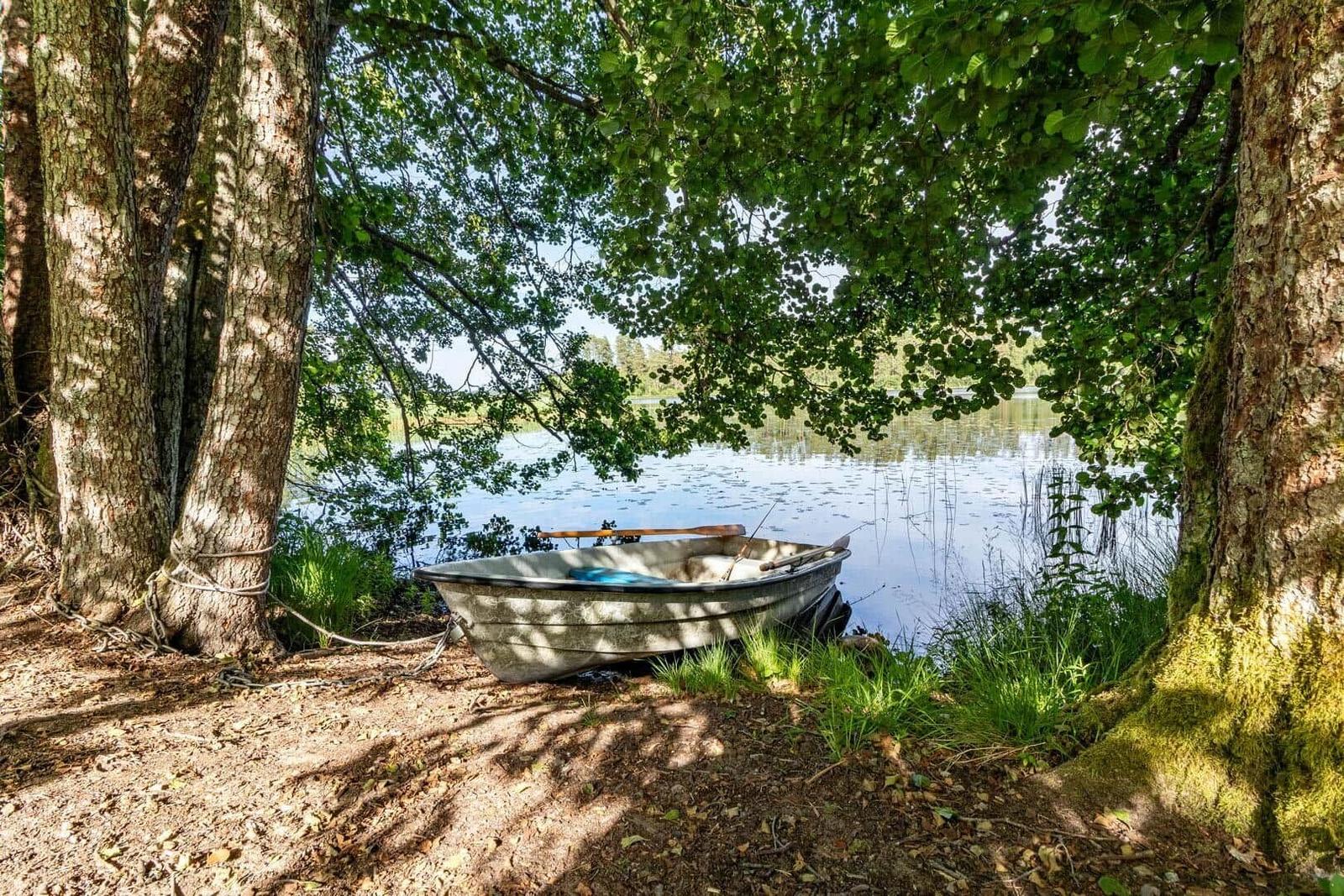 Ein kleines Boot liegt am Ufer eines Sees unter Bäumen.