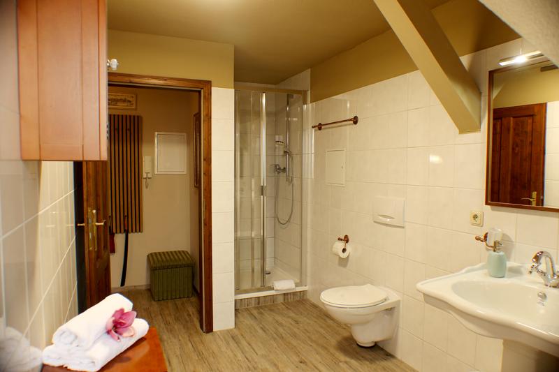 Badezimmer mit Dusche, Toilette und Waschbecken. Holzboden und weiße Fliesen.