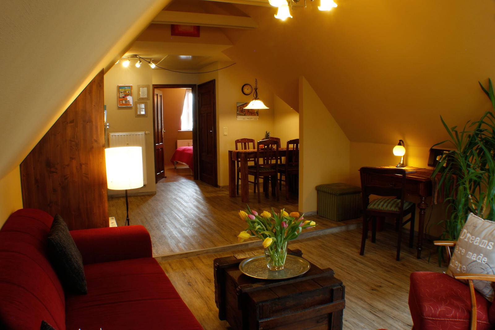 Wohn- und Essbereich mit Sofa, Tisch, Stühlen und Schreibtisch unter Holzdach.