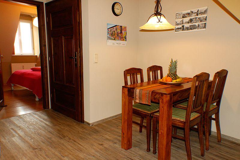 Esszimmer mit Holztisch, Stühlen und Obst. Durchgang zur Schlafzimmer mit Bett.