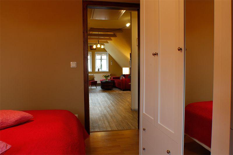 Zimmer mit rotem Bett und Blick in Wohnbereich mit Sofa und Holzboden.