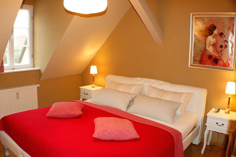 Schlafzimmer mit Dachschrägen, weißem Bett und rotem Deckenbezug.