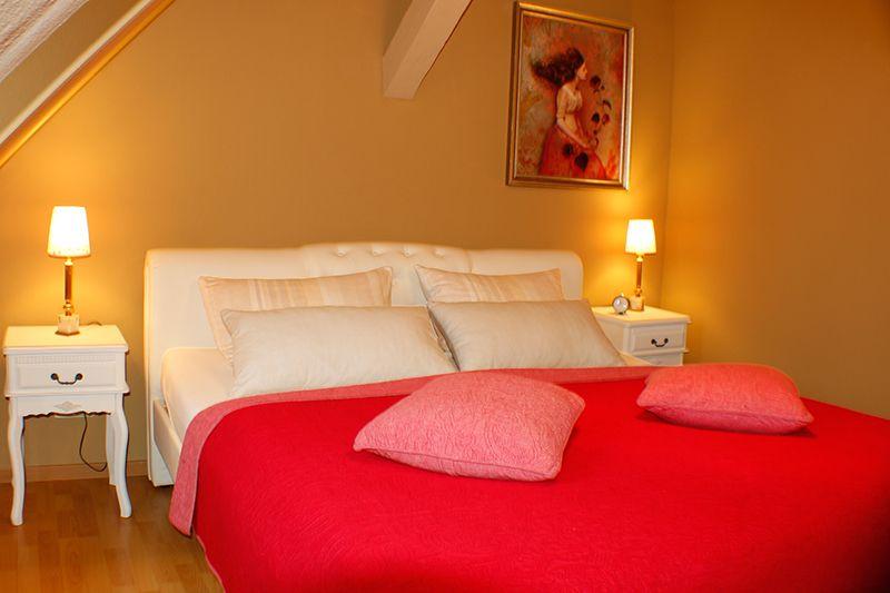 Schlafzimmer mit weißem Bett, rotem Bettlaken und zwei Nachttischen mit Lampen.