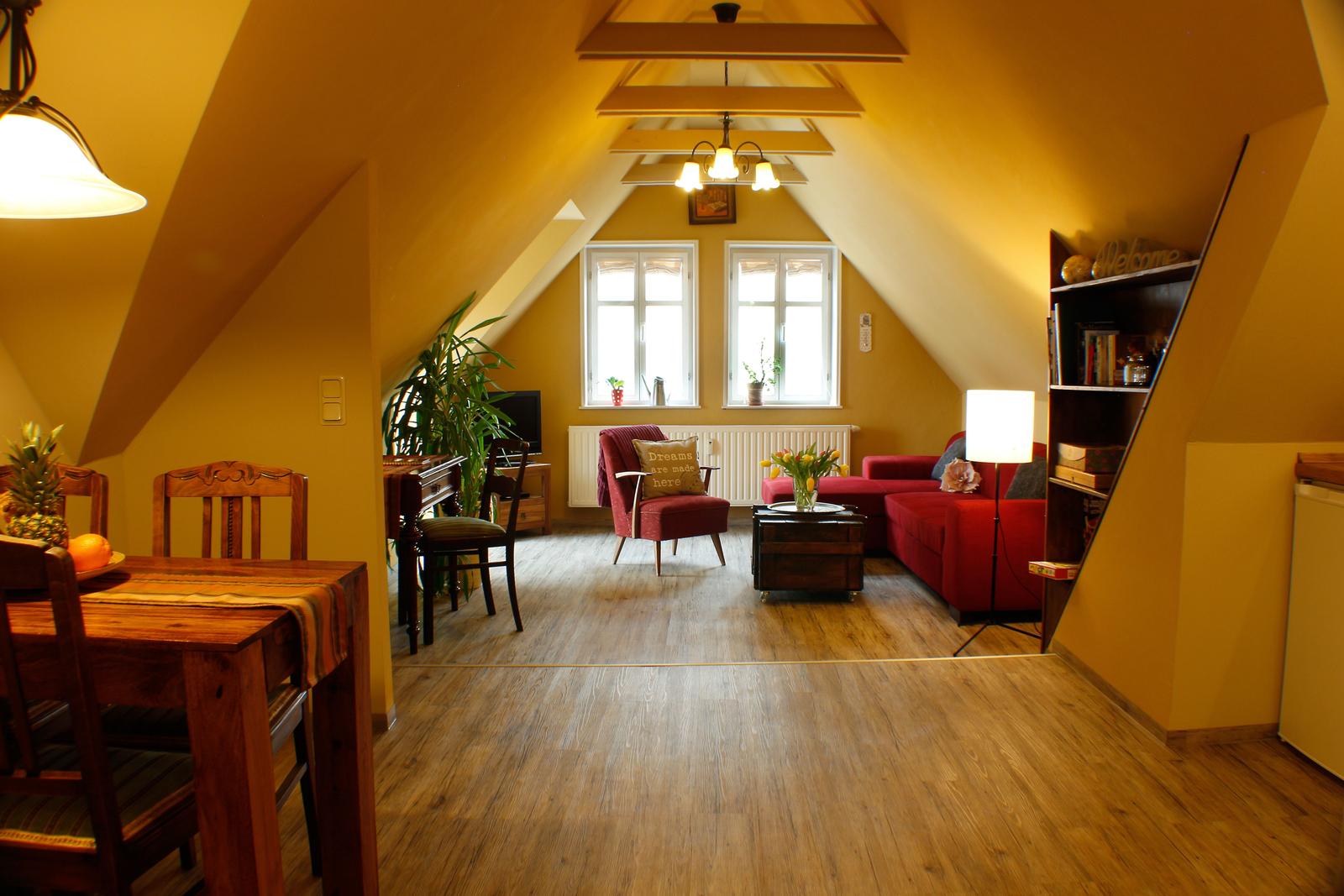 Wohn- und Essbereich mit Holzboden, rotem Sofa und Holztisch. Dachschräge mit Fenstern.