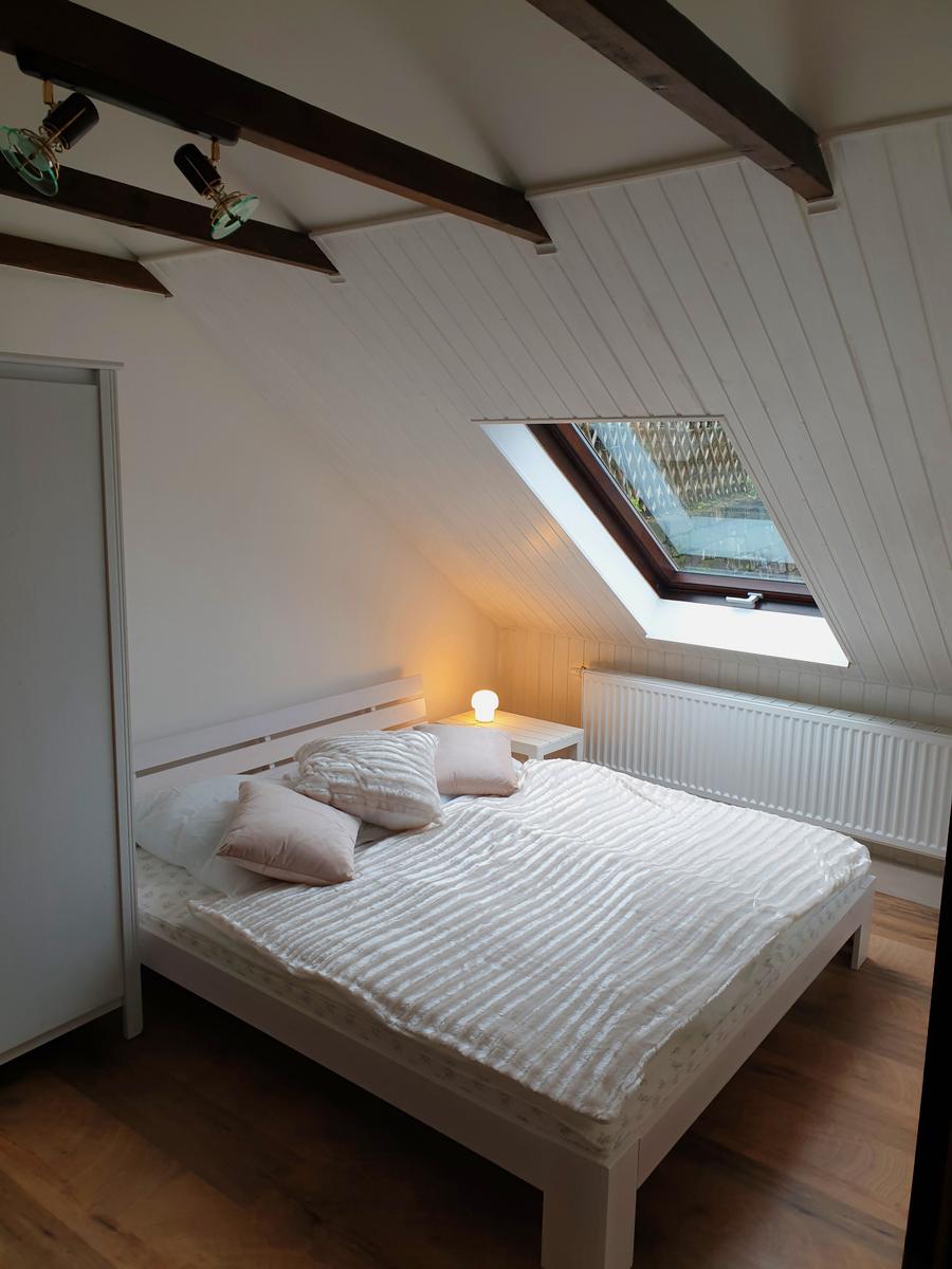 Schlafzimmer mit Dachschrägen, Dachfenster und Holzboden. Bett, Nachttisch und Heizung sind sichtbar.