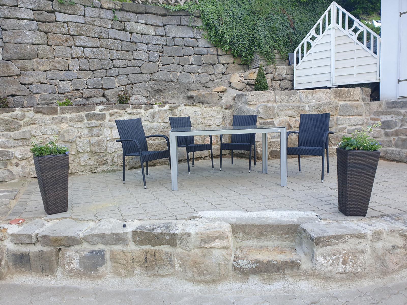 Terrasse mit Tisch und vier Stühlen, Steinmauern und Pflanzen