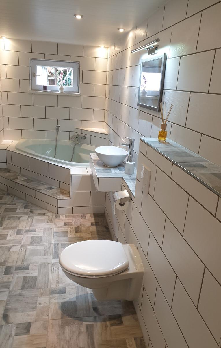 Badezimmer mit Badewanne, Waschbecken und Toilette. Fliesenwand und Holzoptikboden.