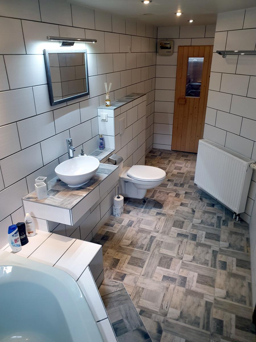 Badezimmer mit Waschbecken, Toilette und Badewanne. Fliesenboden und Wandfliesen.
