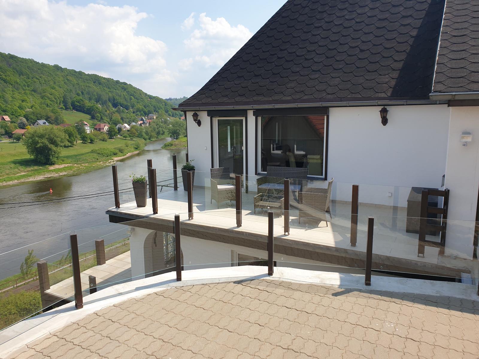 Terrasse mit Sitzgelegenheiten und Blick auf Fluss und Hügel.