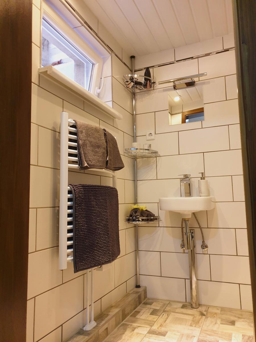 Badezimmer mit Dusche, Waschbecken und Heizkörper. Weiße Fliesen und Holzboden.