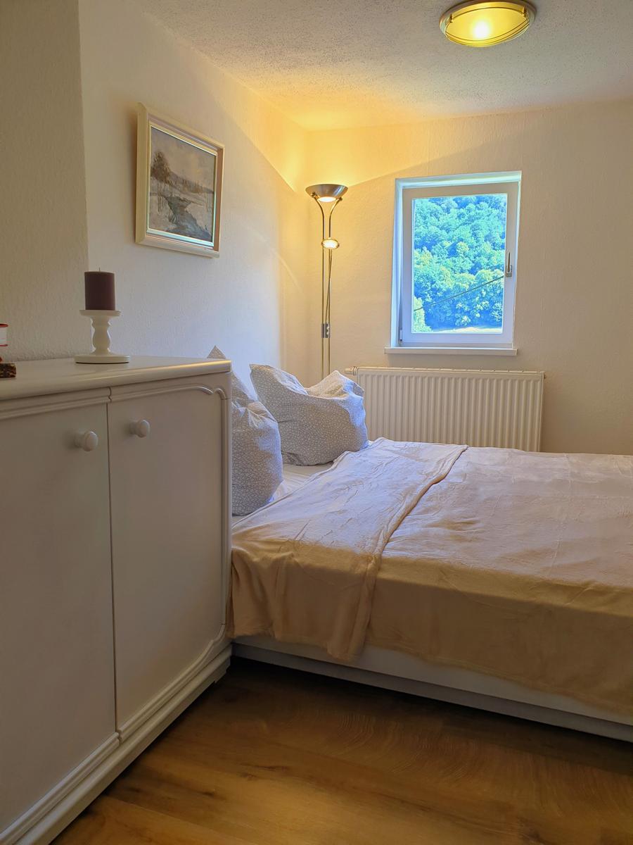 Schlafzimmer mit Bett, Schrank, Fenster und Stehlampe.