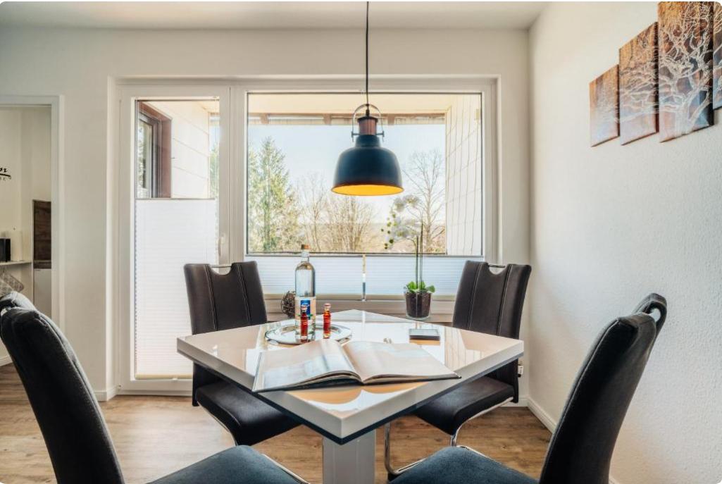 Esszimmer mit quadratischem Tisch, schwarzen Stühlen und Blick auf Außenbereich.