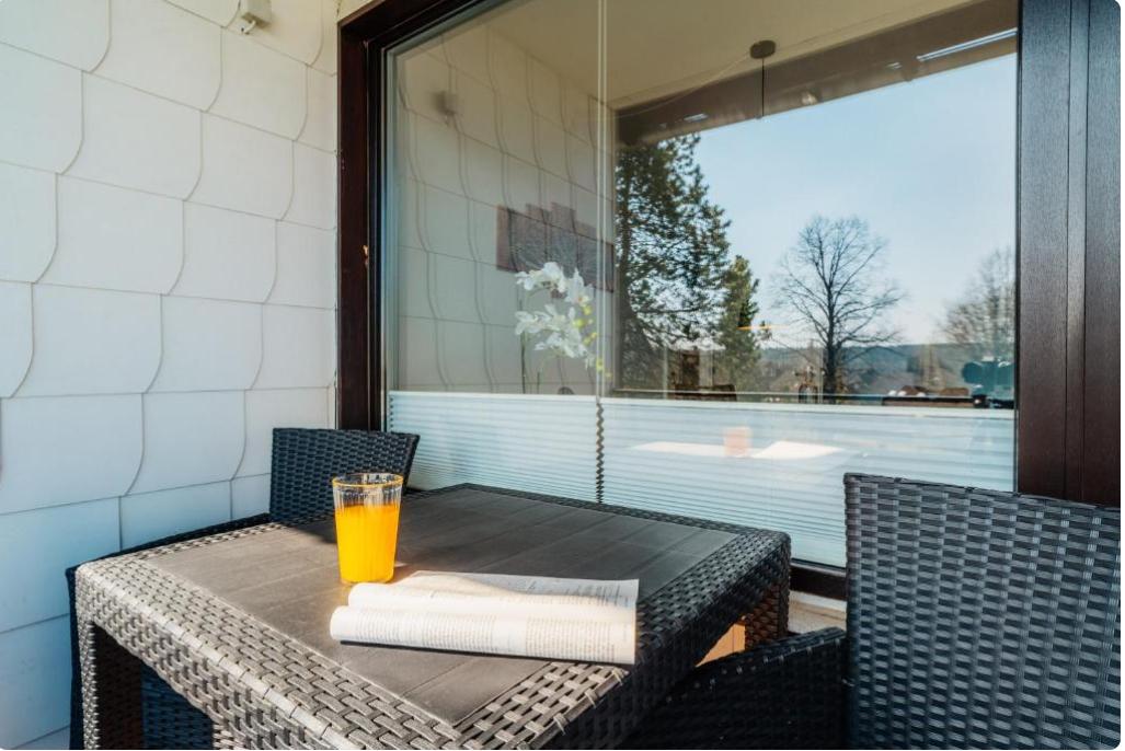 Terrasse mit Tisch, Stühlen und Glas. Im Hintergrund sind Bäume und ein Fenster sichtbar.