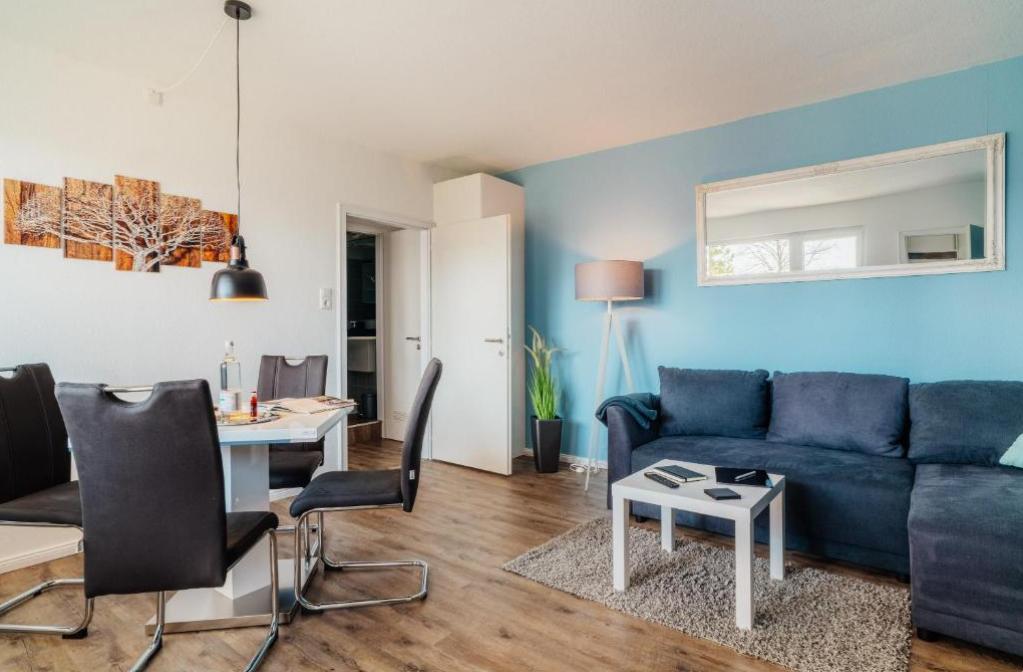 Wohn- und Essbereich mit Sofa, Tisch und Stühlen. Blaue Wand, Spiegel und Pflanze.