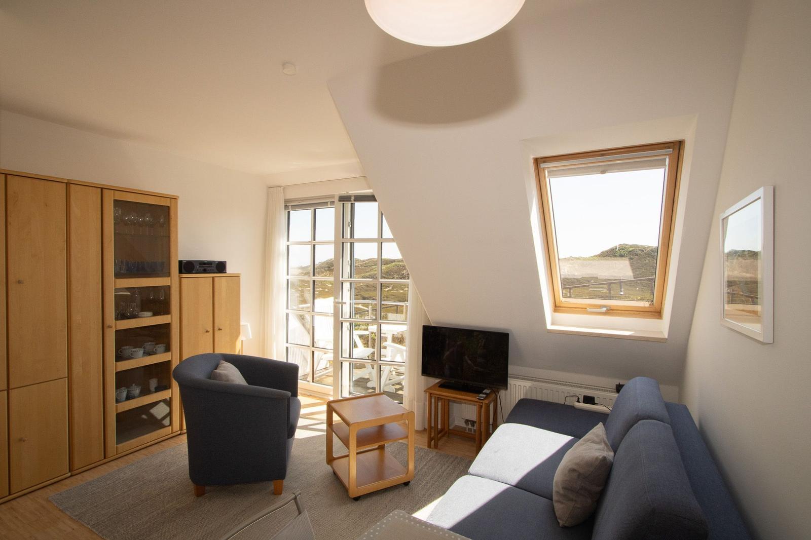 Living room with sofa, armchair, TV, and windows with views.