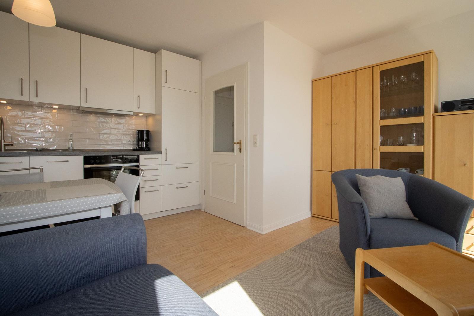 Living kitchen with blue sofa, wooden furniture, and kitchen cabinets.