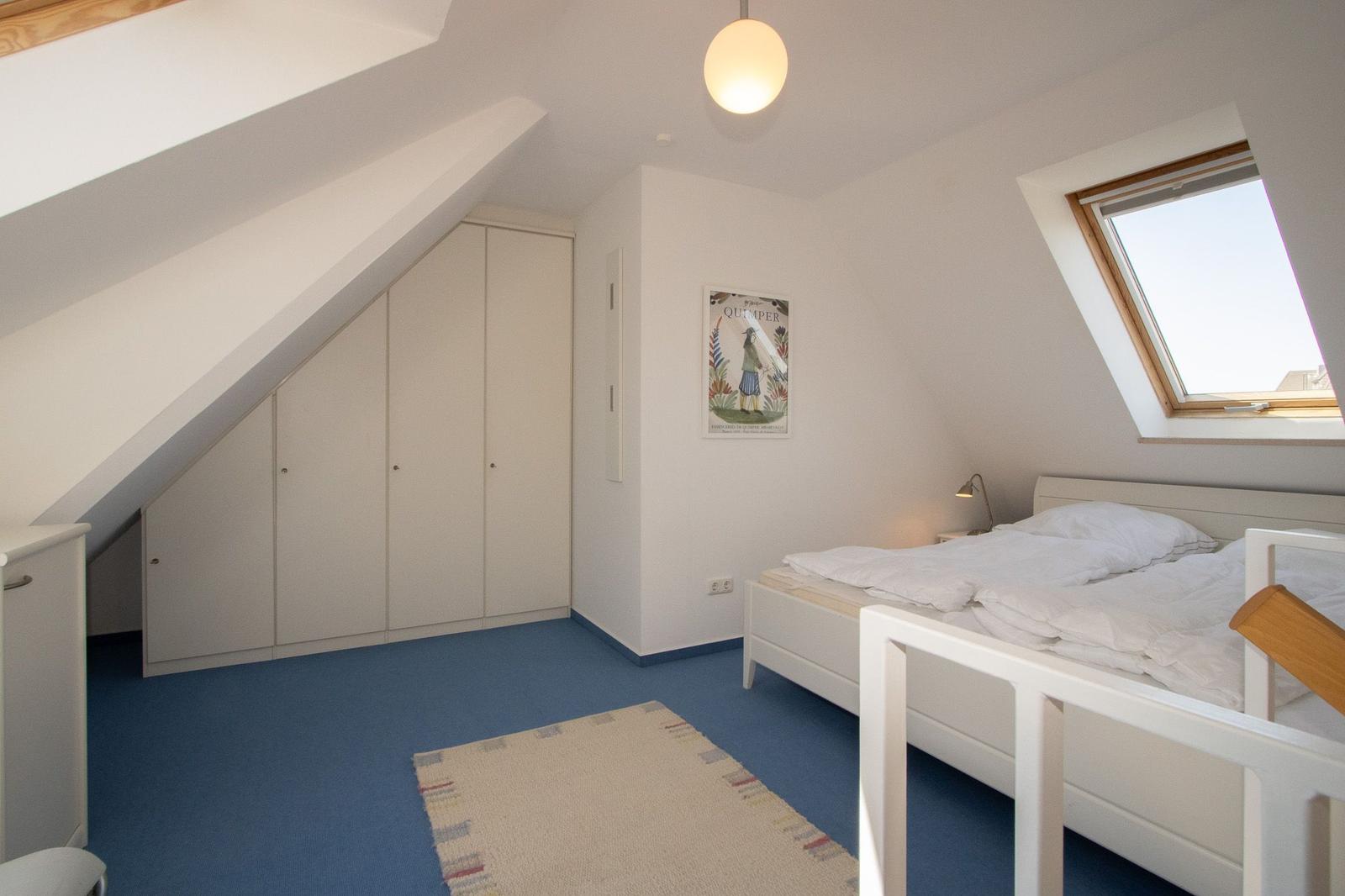 Bedroom with sloped ceiling, skylight, bed, and wardrobe.