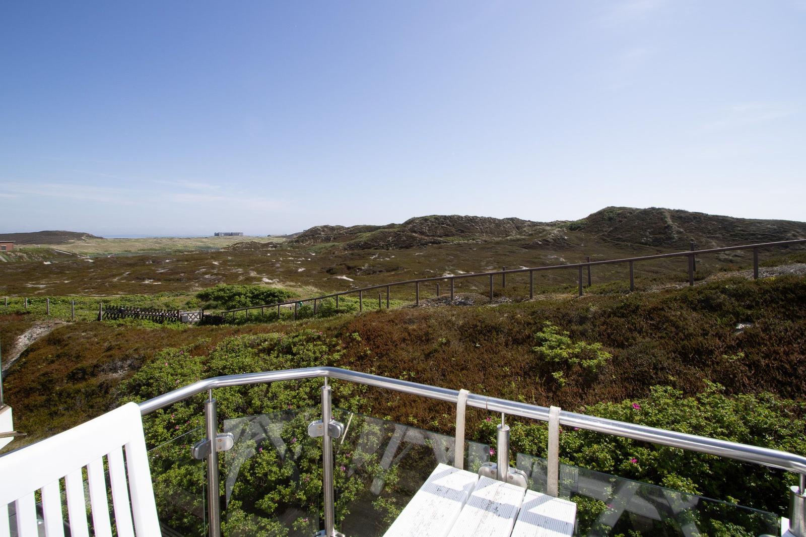 Terrace with glass railing and white chair, view of hills and horizon.