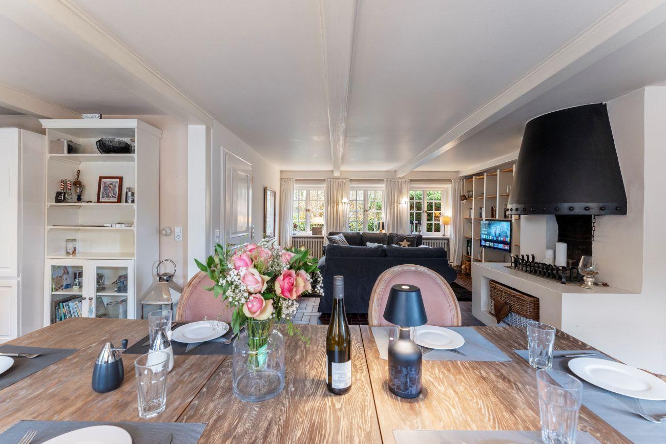 Essbereich mit Holztisch, Blumen und Fernseher im Hintergrund.