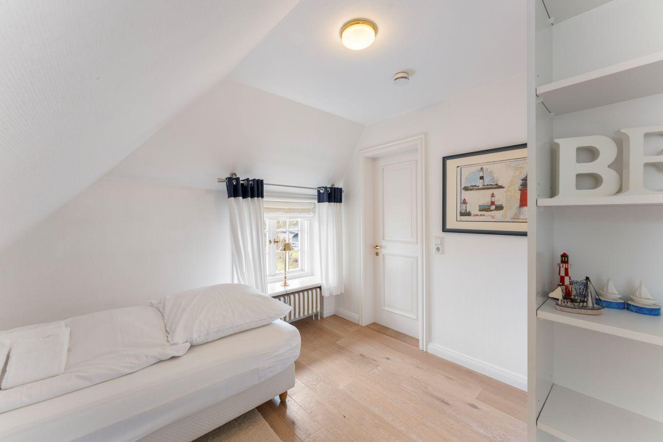 Schlafzimmer mit Dachschräge, Fenster, Bett und Regal mit Dekoration.
