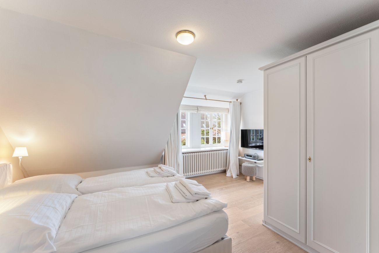 Schlafzimmer mit Doppelbett, Kleiderschrank und Fenster. TV und Heizung sind vorhanden.