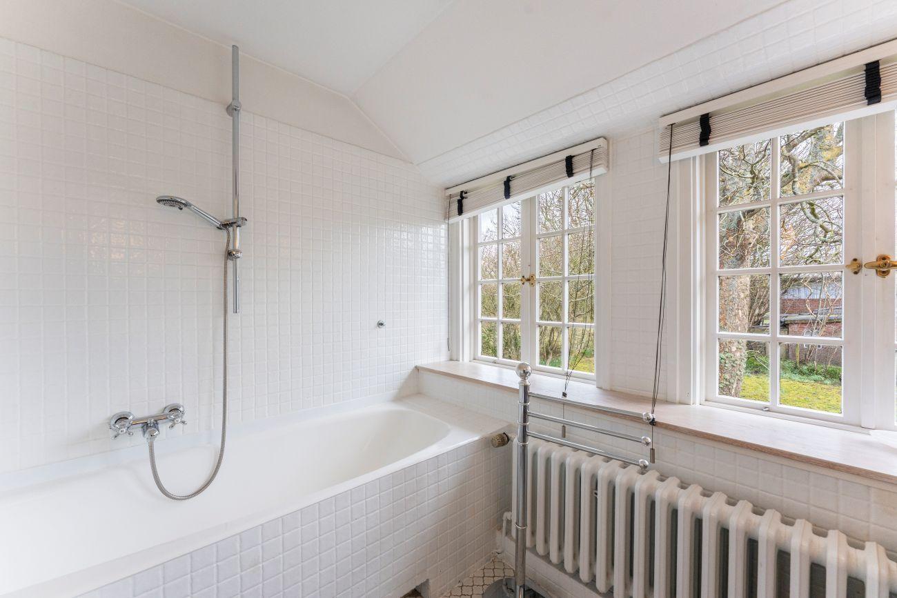 Bad mit Badewanne, Dusche und zwei Fenstern mit Blick auf den Garten.