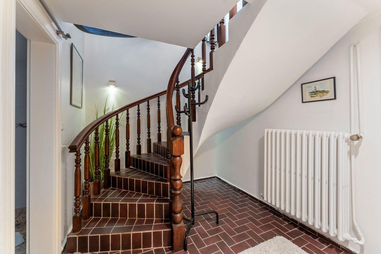 Holzgetreppe mit Geländer führt zur oberen Etage. Wandheizung und Bild an der Wand.