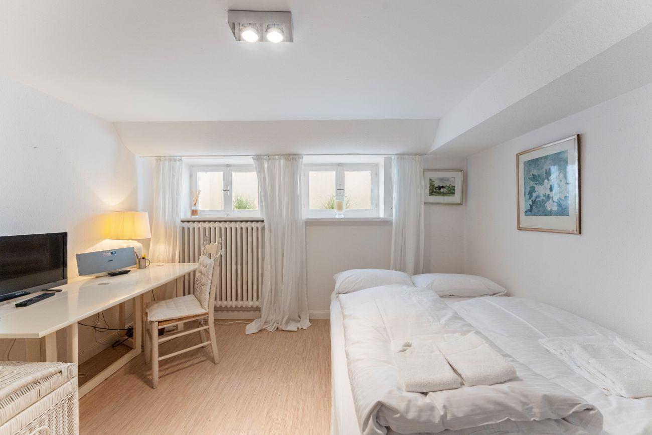 Ein Schlafzimmer mit Bett, Schreibtisch, Fernseher und Fenster mit Vorhängen.