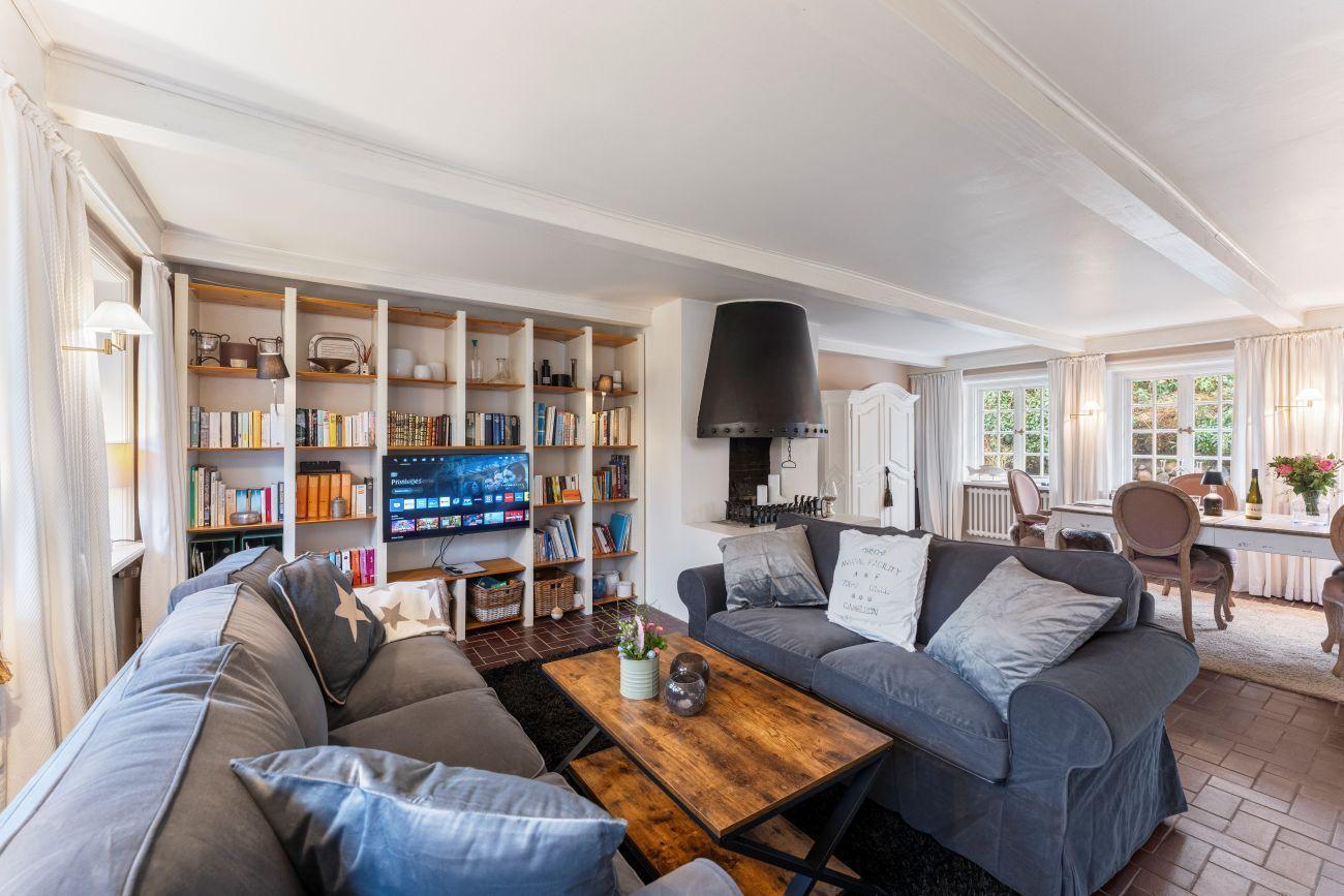 Wohnzimmer mit Sofa, Fernseher und Bücherregal. Kamin und Essbereich sind sichtbar.