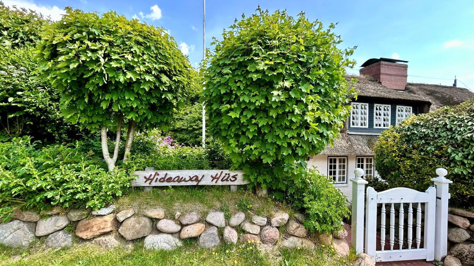 Haus mit Strohdach und Schild Hideaway Hüs im grünen Garten.