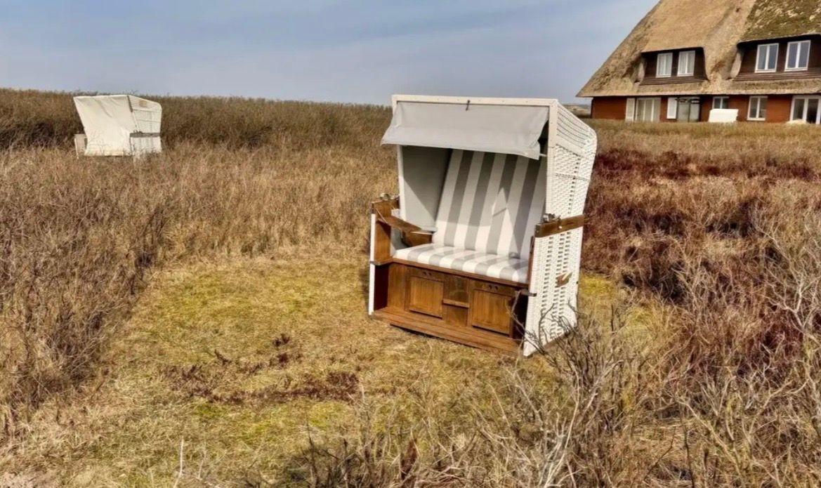 Strandkorb mit Streifenbezug steht im Gras vor einem Haus.