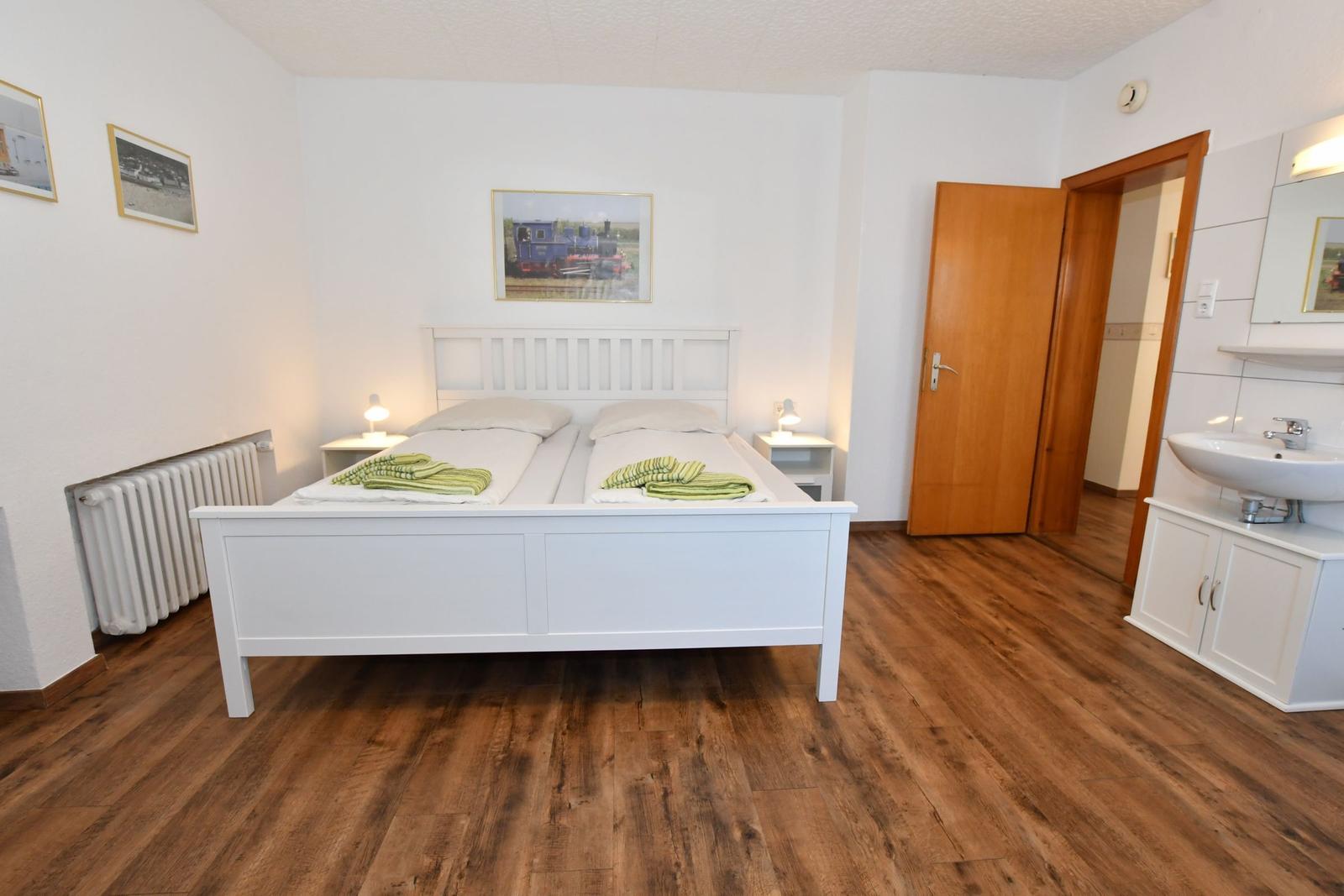 Schlafzimmer mit Doppelbett, Holzboden und Bad. Wandbilder und Nachttische.