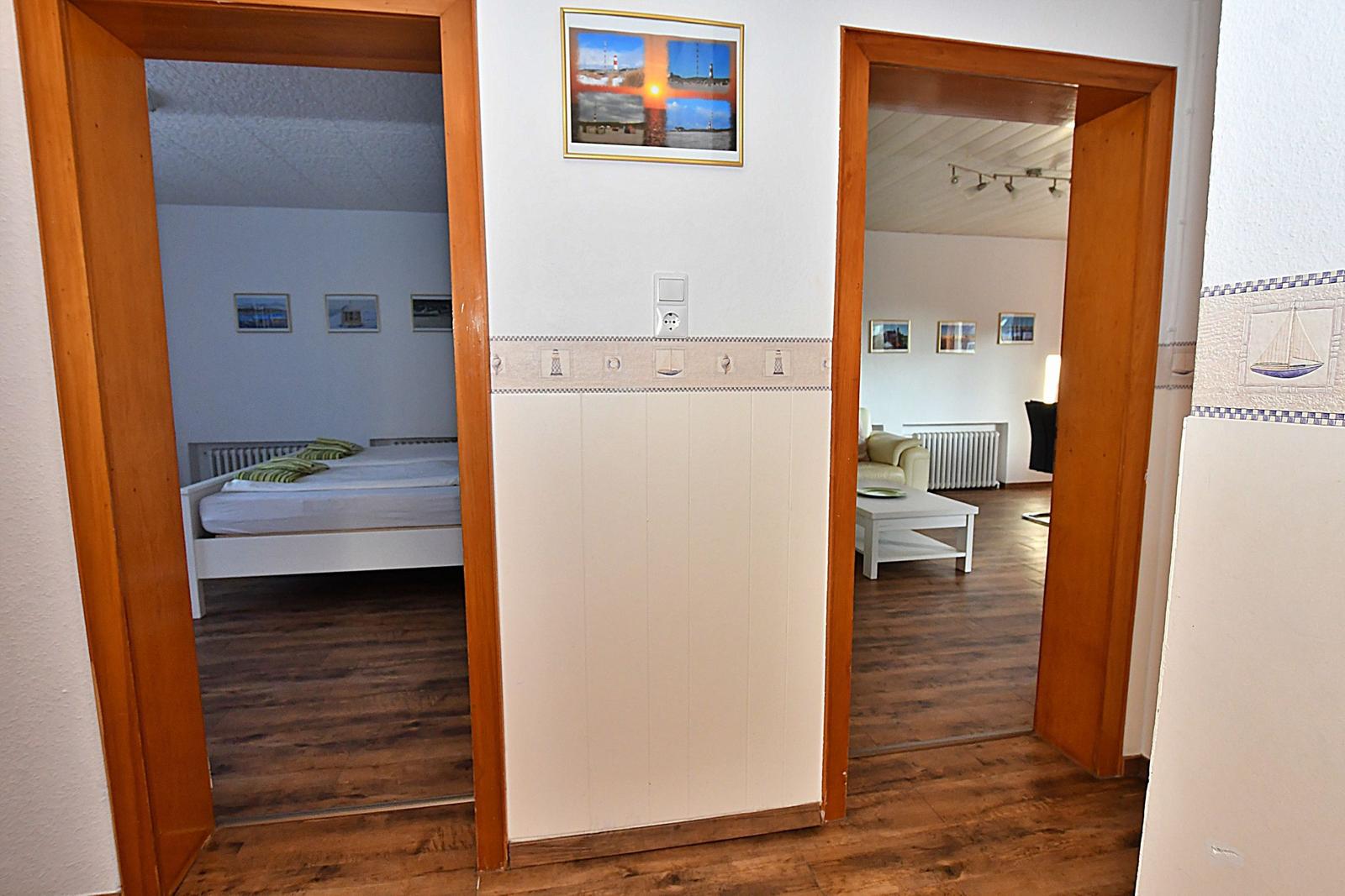 Zwei Räume sind über Türöffnungen sichtbar. Ein Schlafzimmer mit Bett und Wohnzimmer mit Sofa.