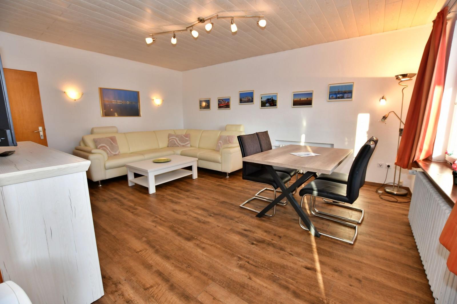 Wohn- und Essbereich mit Sofa, Tisch und Stühlen. Holzboden und weiße Wände.