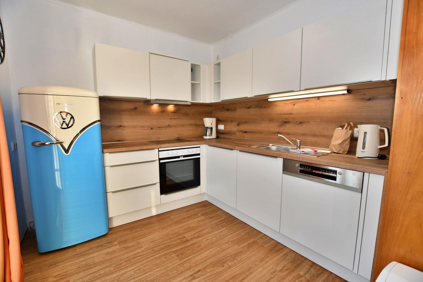 Küche mit weißen Schränken, Holz Arbeitsplatte und blau-weißem Kühlschrank.