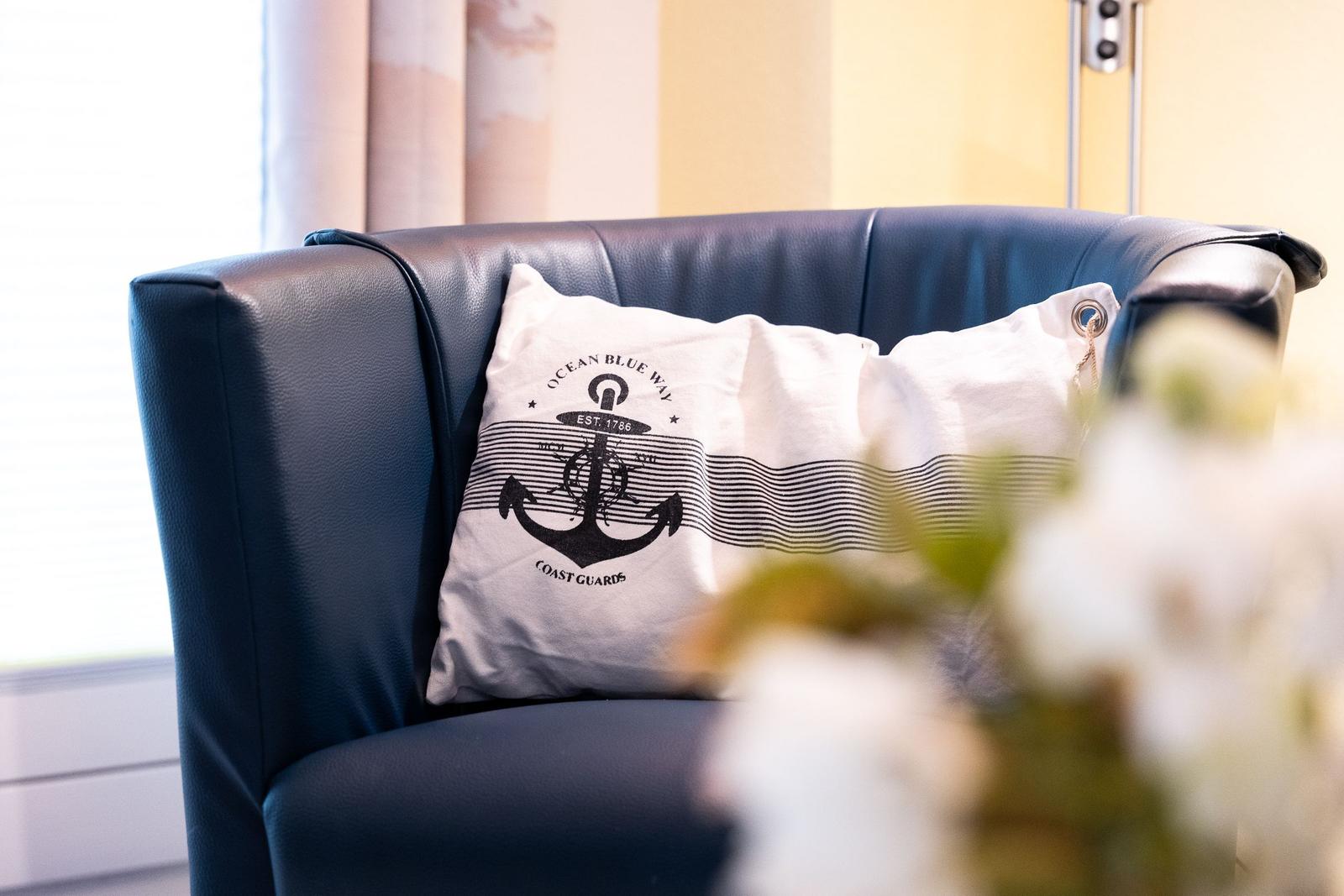 A dark blue leather armchair with a white cushion featuring an anchor design.