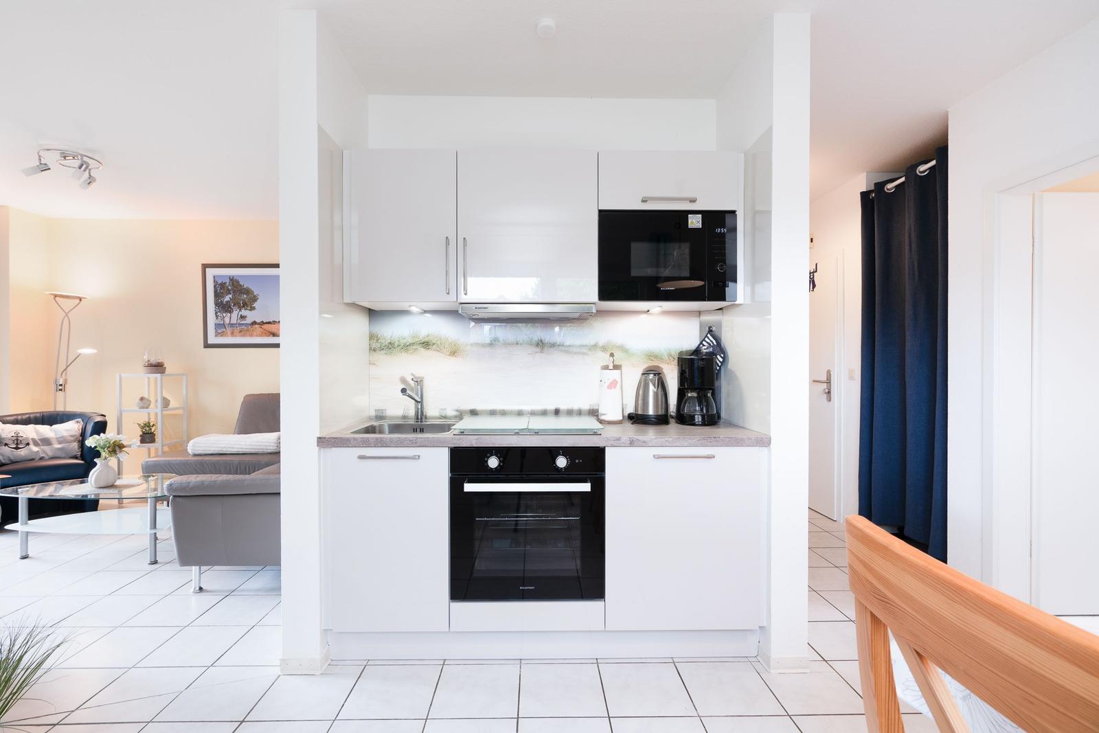 Kitchen with white cabinets, microwave, and oven. Living area with sofa and coffee table visible.