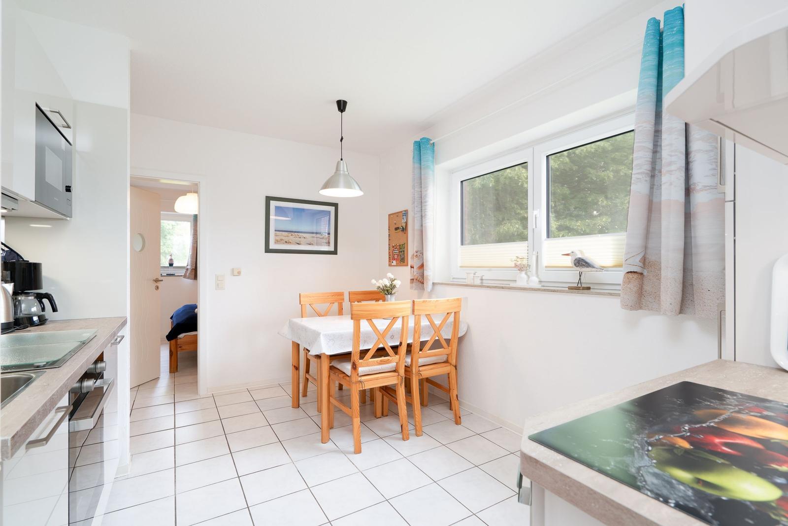 Dining area with wooden table and chairs, window with curtains, and kitchen area.